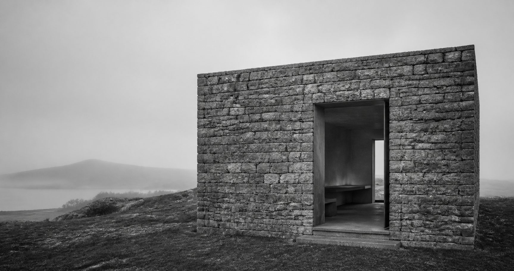 Small rural stone pavilion set into a quiet landscape